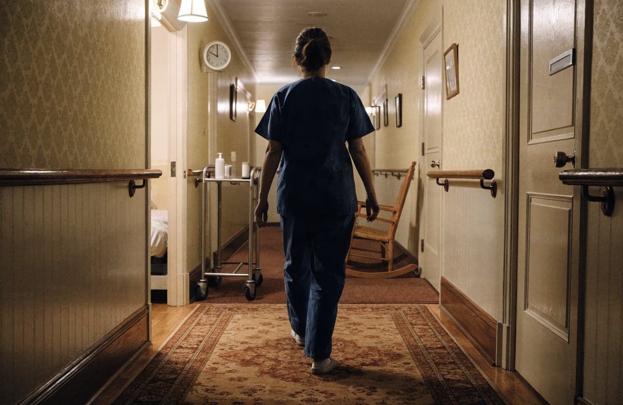 Caregiver in scrubs walking down the hallway of a residential care home at night
