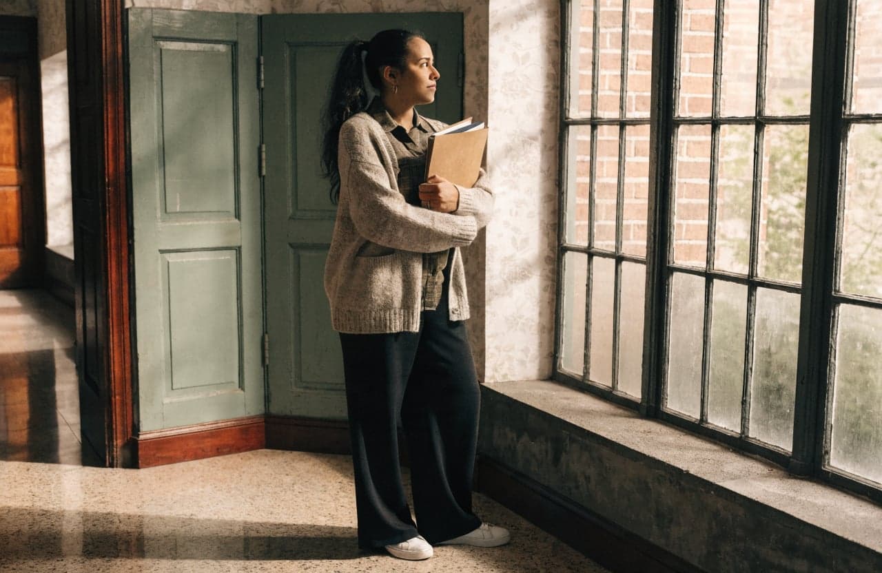 Employee holding work folders alone in an office hallway
